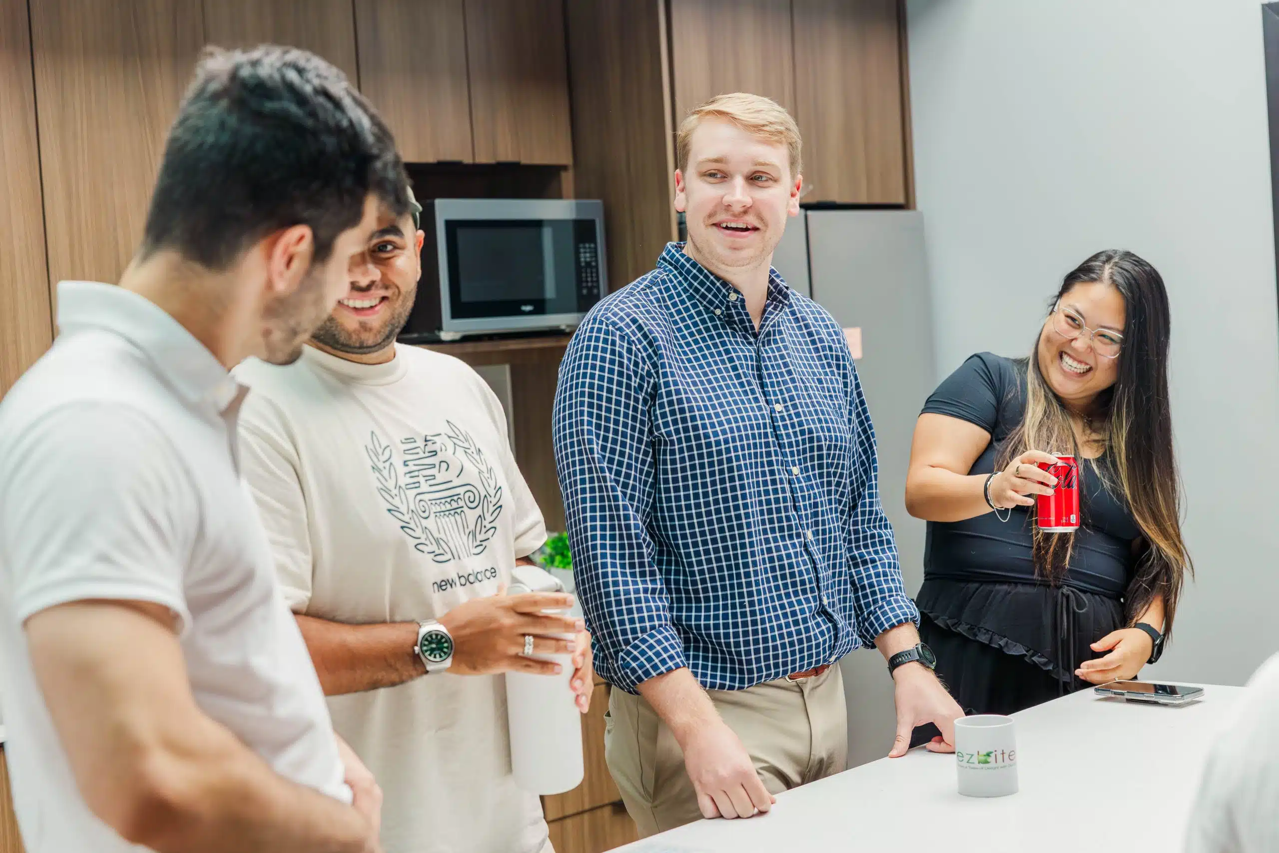 Four Cookie Finance employees laugh and chat together in the office kitchen at Cookie Finance headquarters in Richmond, VA, enjoying a casual break around a counter.