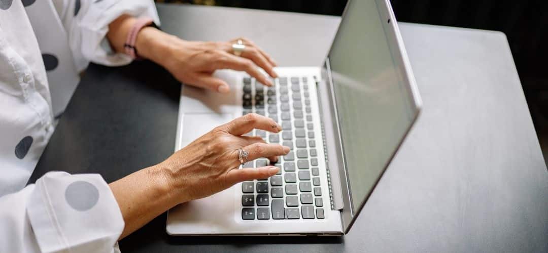 How to Monetize a Blog in 2026 (Multiple Income Streams Guide) (1) Close-up of a woman's hands typing on a silver laptop on a dark desk, wearing rings and a white polka dot blouse