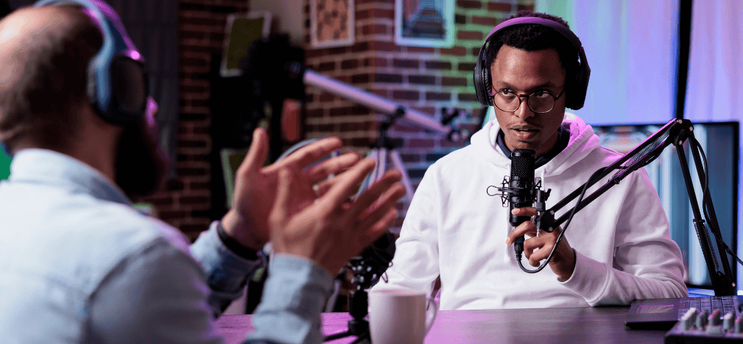 How to become a full time content creator (1) Two men wearing headphones record a podcast in a neon-lit studio, with one speaking into a condenser microphone on a boom arm while the other gestures during conversation.