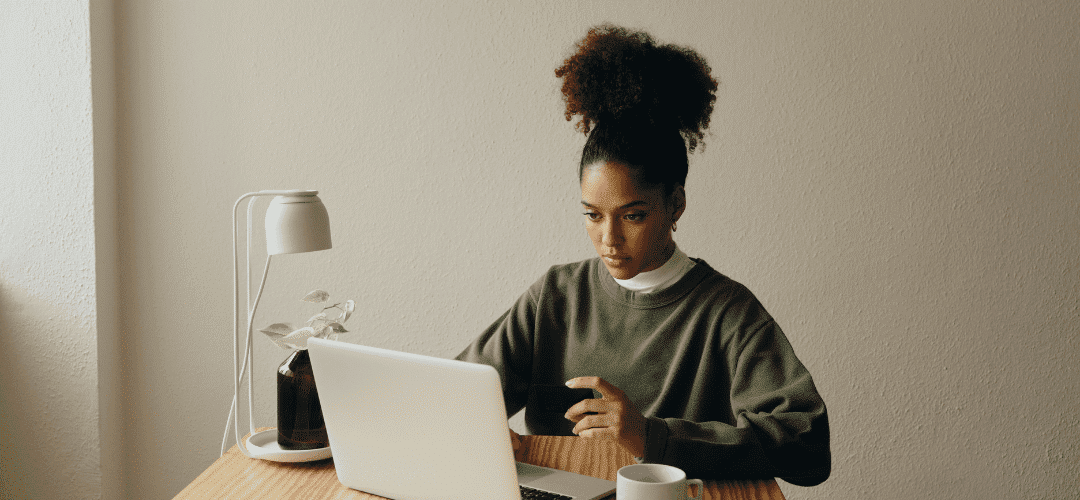 How to set up your LLC A focused young woman with a high bun works on a laptop at a minimal desk with a white lamp, small plant, and coffee cup against a neutral wall.