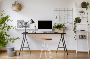 Minimalist home office with a dark trestle desk, iMac, desk lamp, and plants in a bright, airy room.