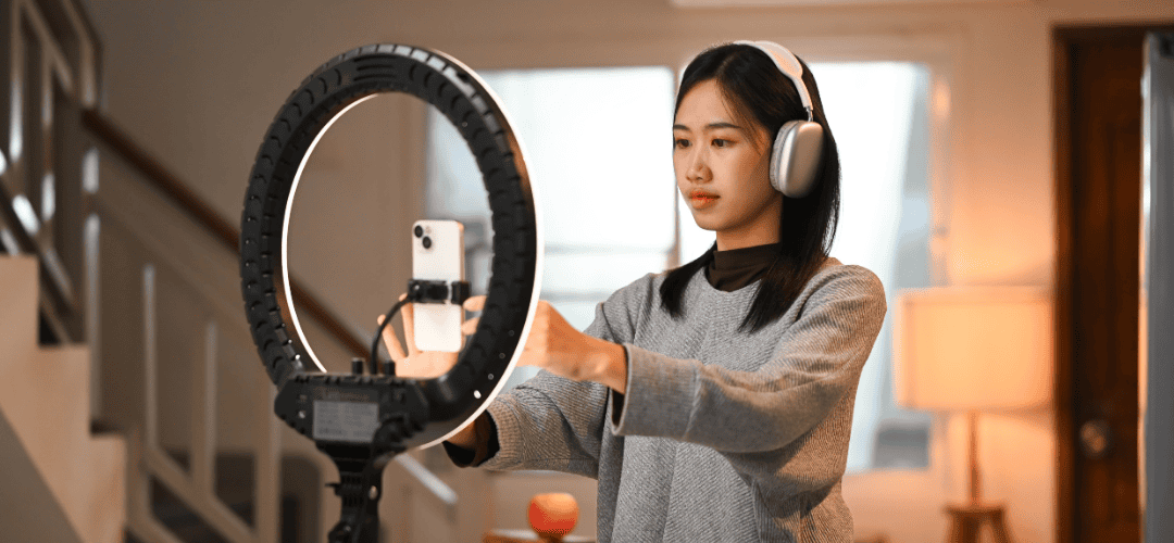 brand deals (1) A woman wearing over-ear headphones adjusts a smartphone mounted in front of a lit ring light, preparing to record or stream for her brand deals.