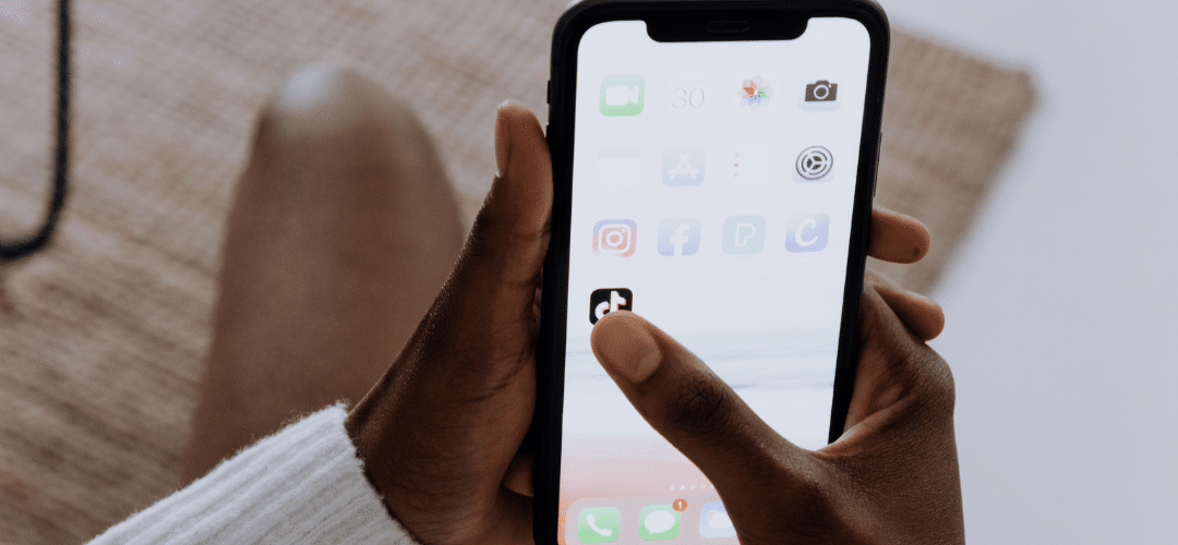 tiktok beginner to pro A person taps the TikTok app on an iPhone home screen displaying various social media icons including Instagram and Facebook.