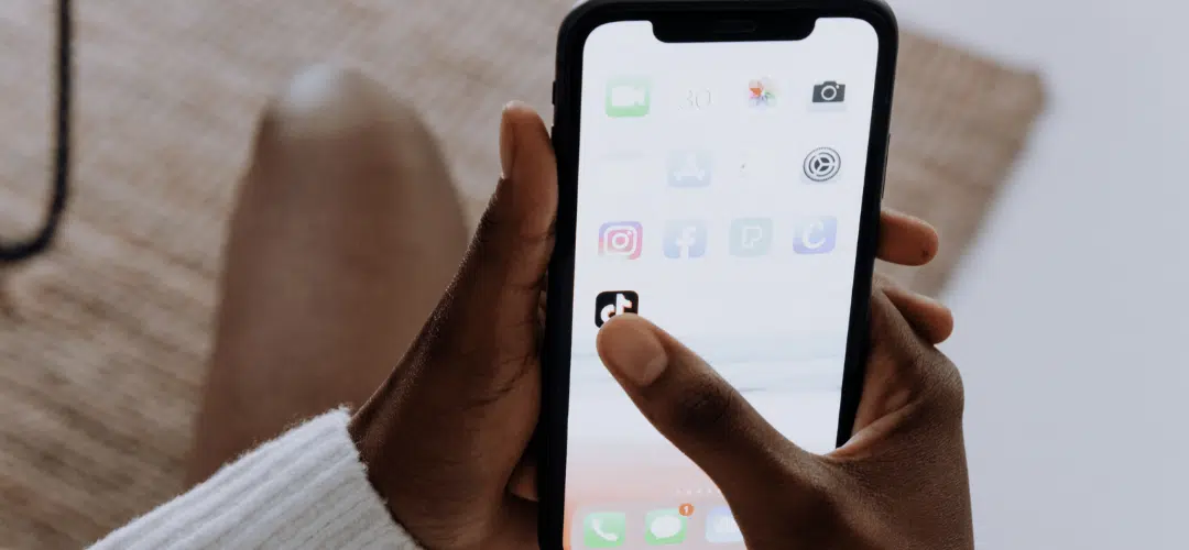 tiktok beginner to pro A person taps the TikTok app on an iPhone home screen displaying various social media icons including Instagram and Facebook.